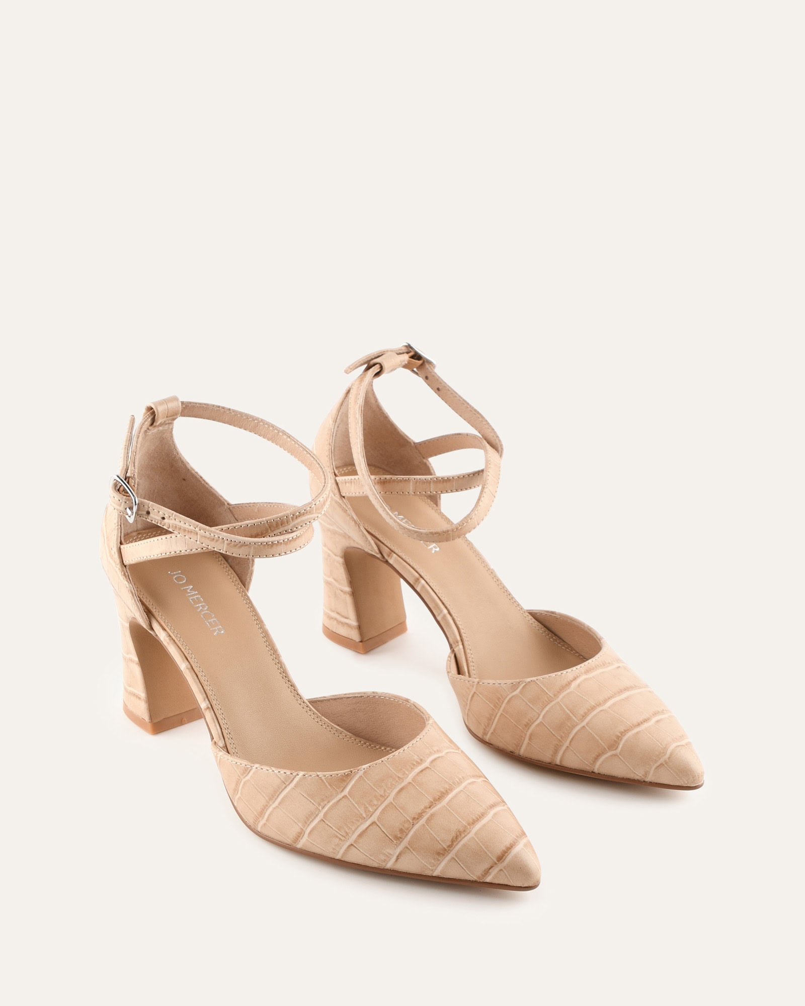 Beige high-heeled shoe with an ankle strap on a light beige background