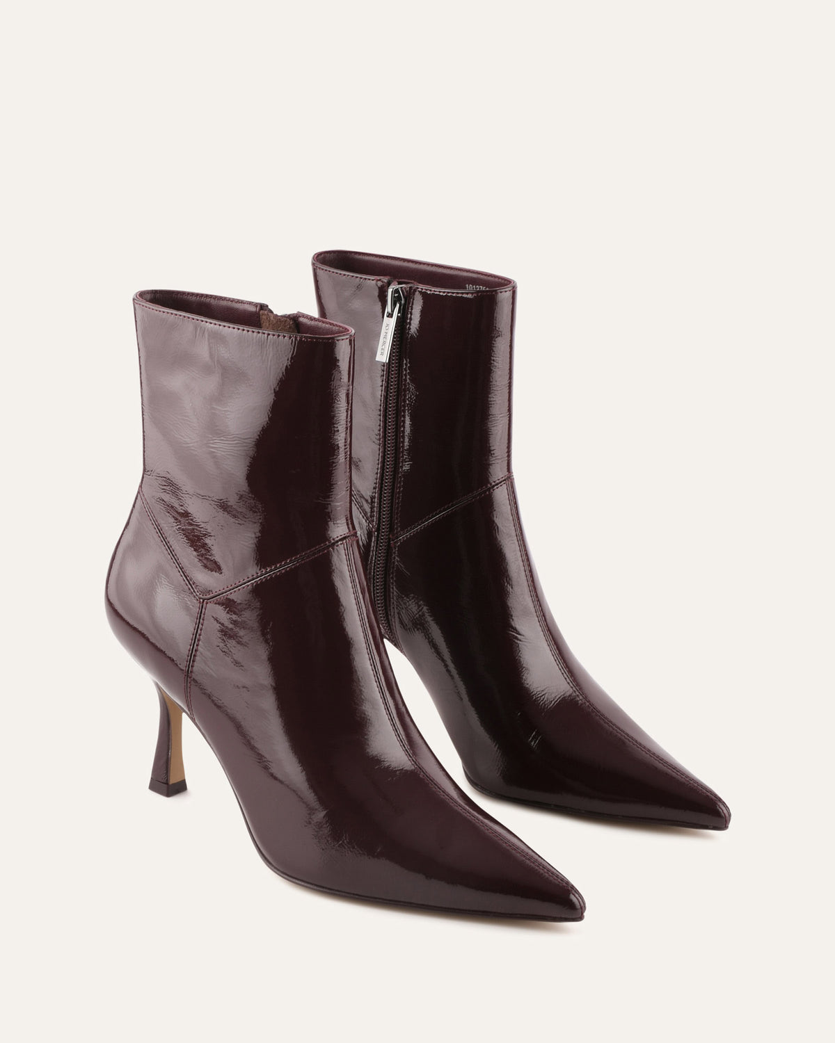 Pair of dark brown patent leather ankle boots on a light beige background