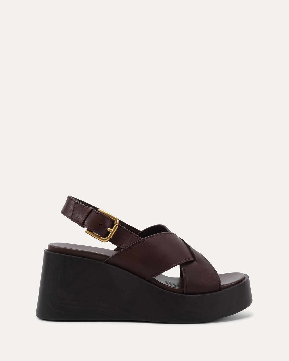 A dark brown platform wedge sandal with crisscrossing straps, an ankle strap with a gold buckle, and a chunky black sole, shown against a light beige background.