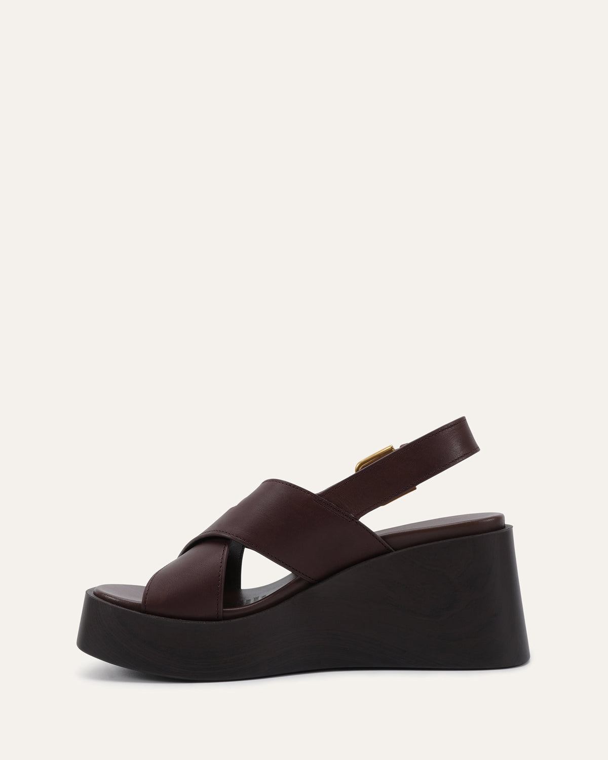 A dark brown platform wedge sandal with crisscrossing straps and a small gold buckle, shown from a side profile on a light off-white background.