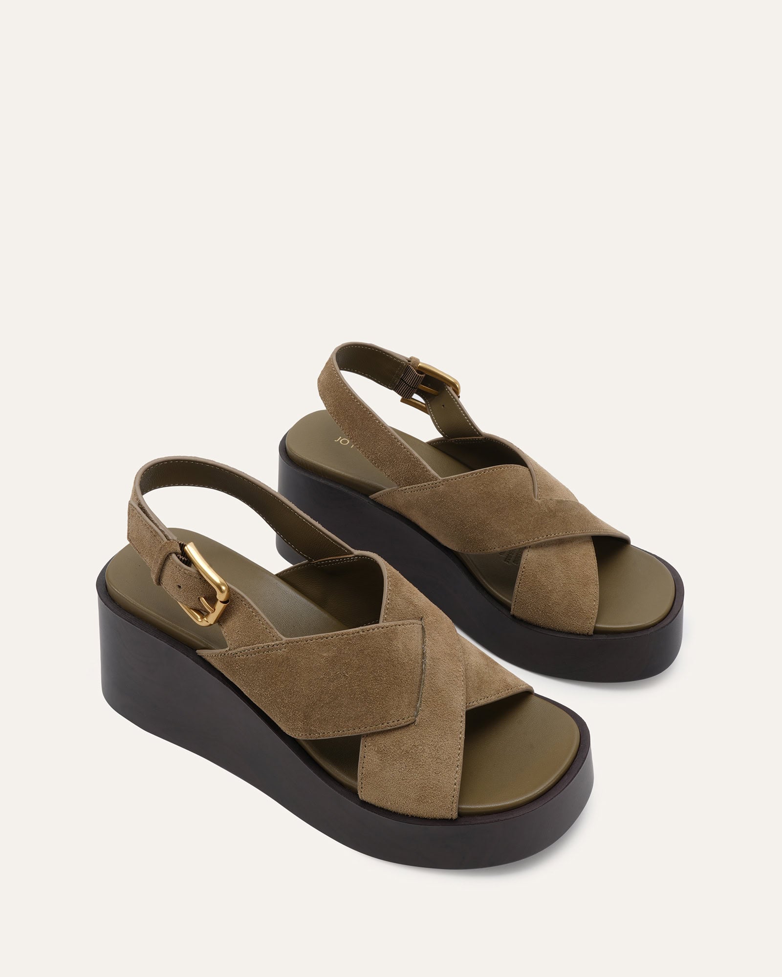 A single platform wedge sandal in taupe suede with a black sole and a gold buckle, shown from a side profile on a light off-white background.