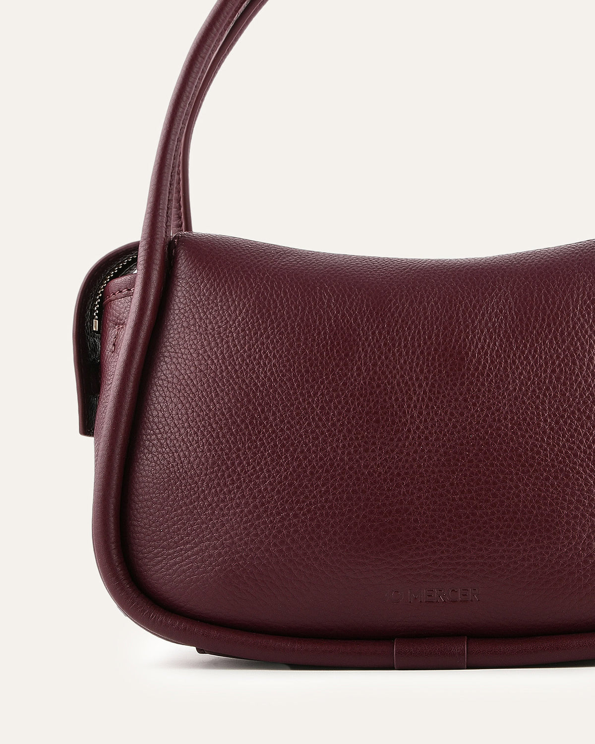 Close-up of a maroon handbag with a visible brand logo on a light background