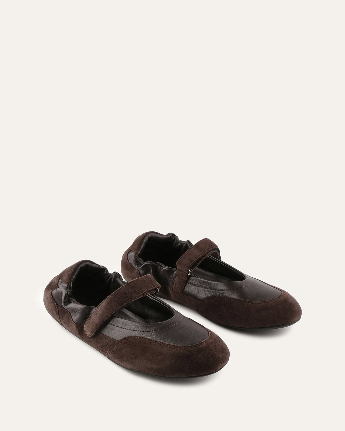 Pair of brown suede shoes with a strap on a light beige background
