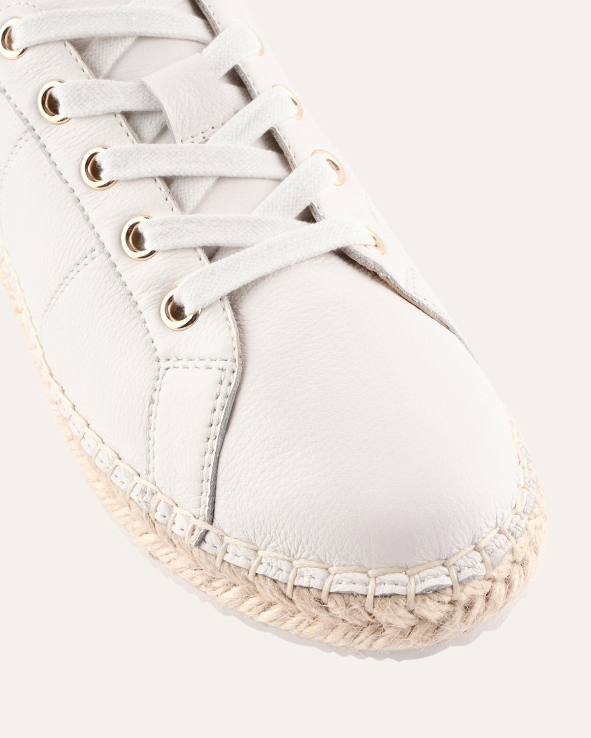 White espadrille shoe with gold eyelets on a white background