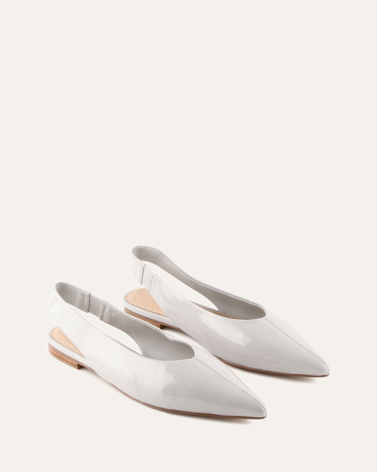 Pair of white pointed-toe flats on a light beige background