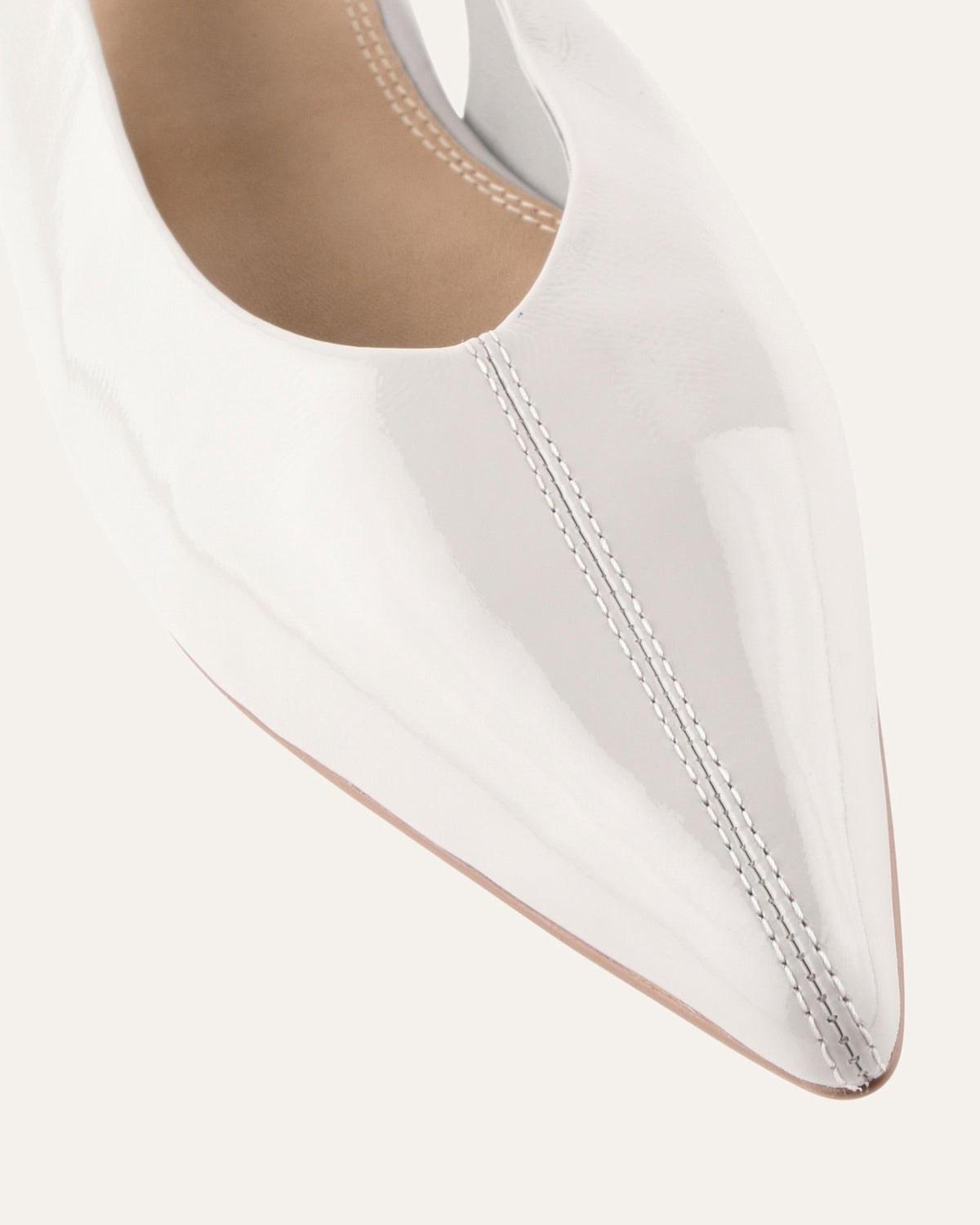 Close-up of a white pointed-toe shoe with visible stitching on a light gray background