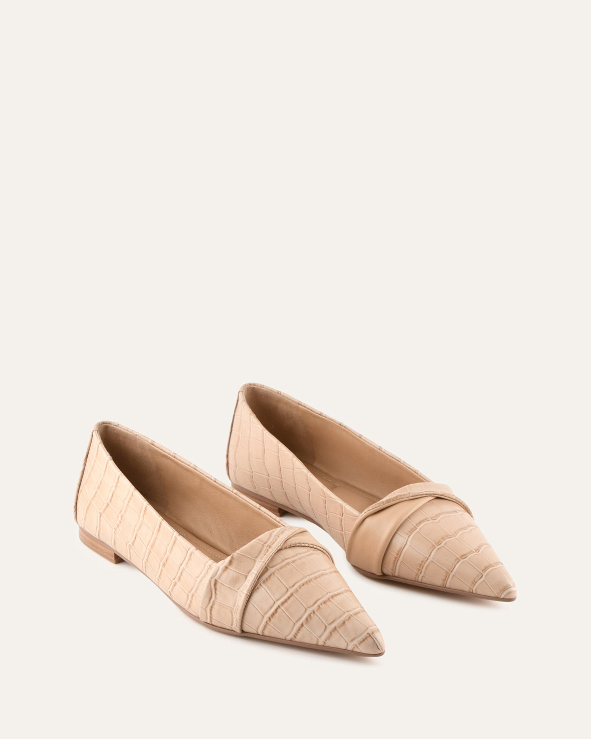 Pair of beige pointed-toe flats on a light beige background