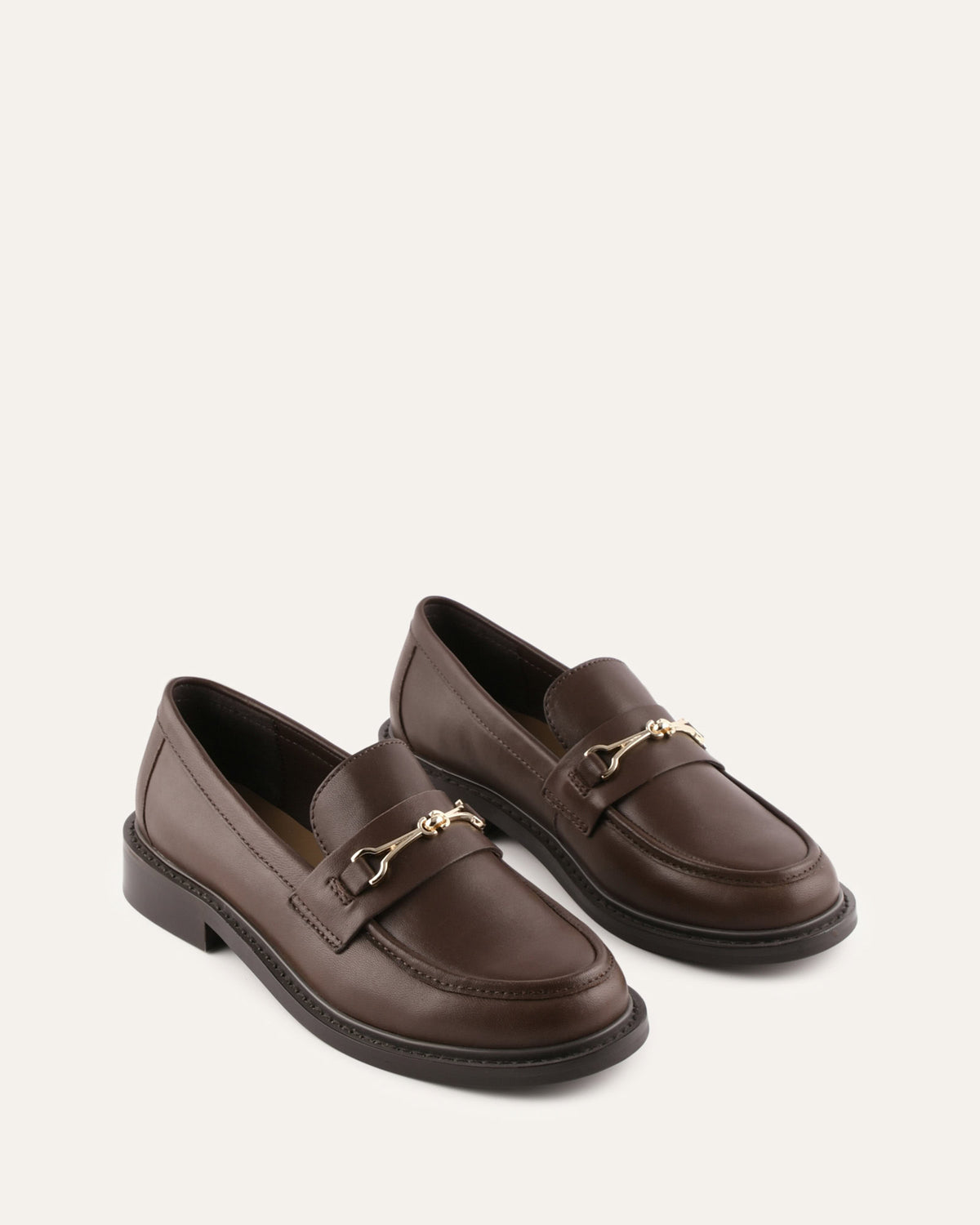 Pair of brown loafers with gold chain details on a beige background