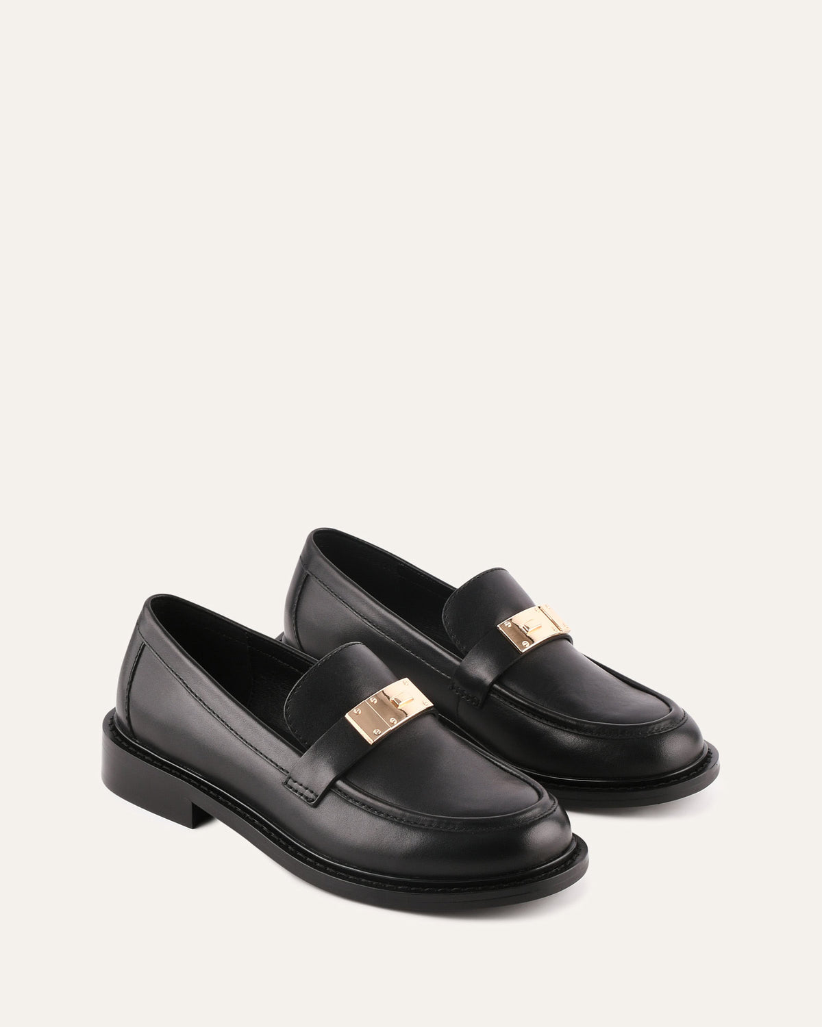 Black loafers with gold accents on a white background