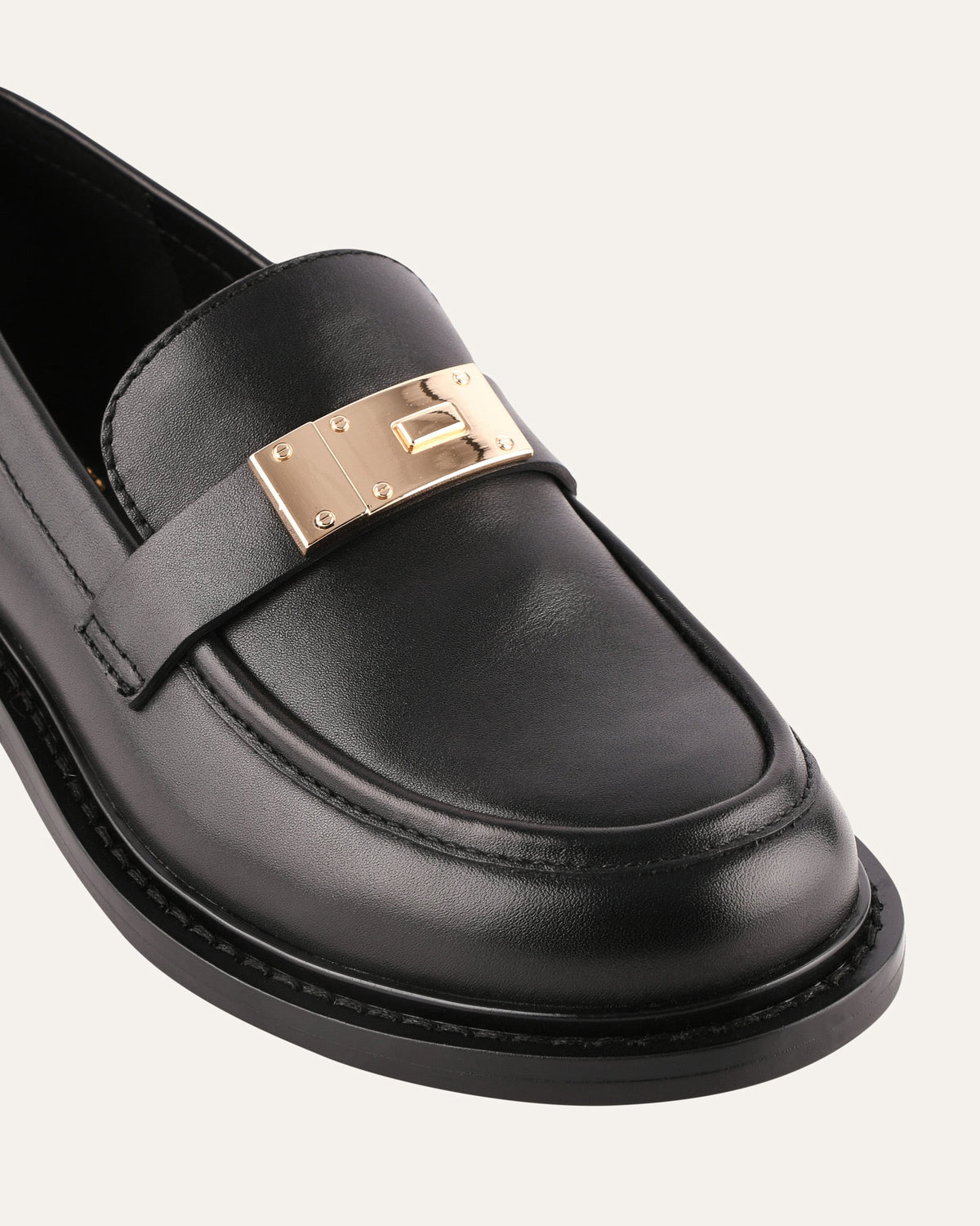 Black loafer with gold buckle on a light gray background