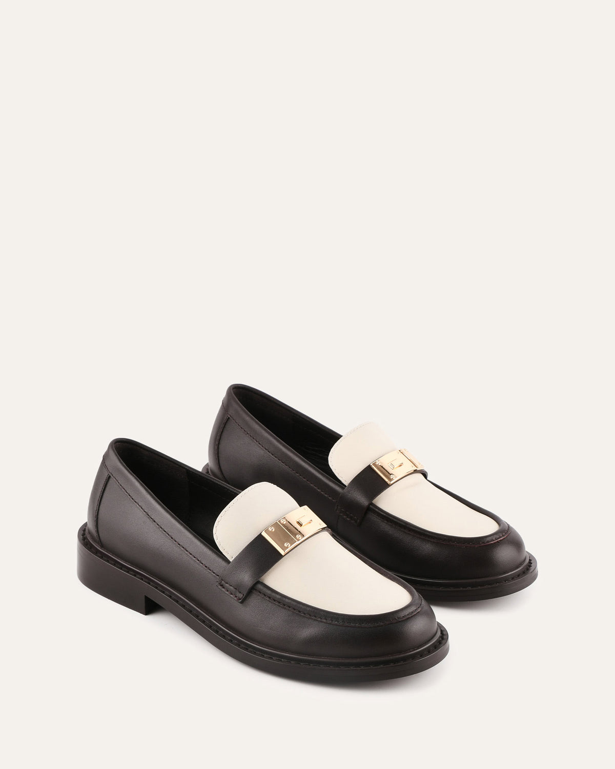Black and white loafers with gold accents on a light beige background