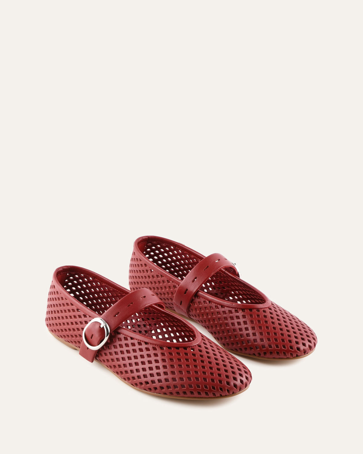 Pair of red perforated shoes with a strap on a light beige background