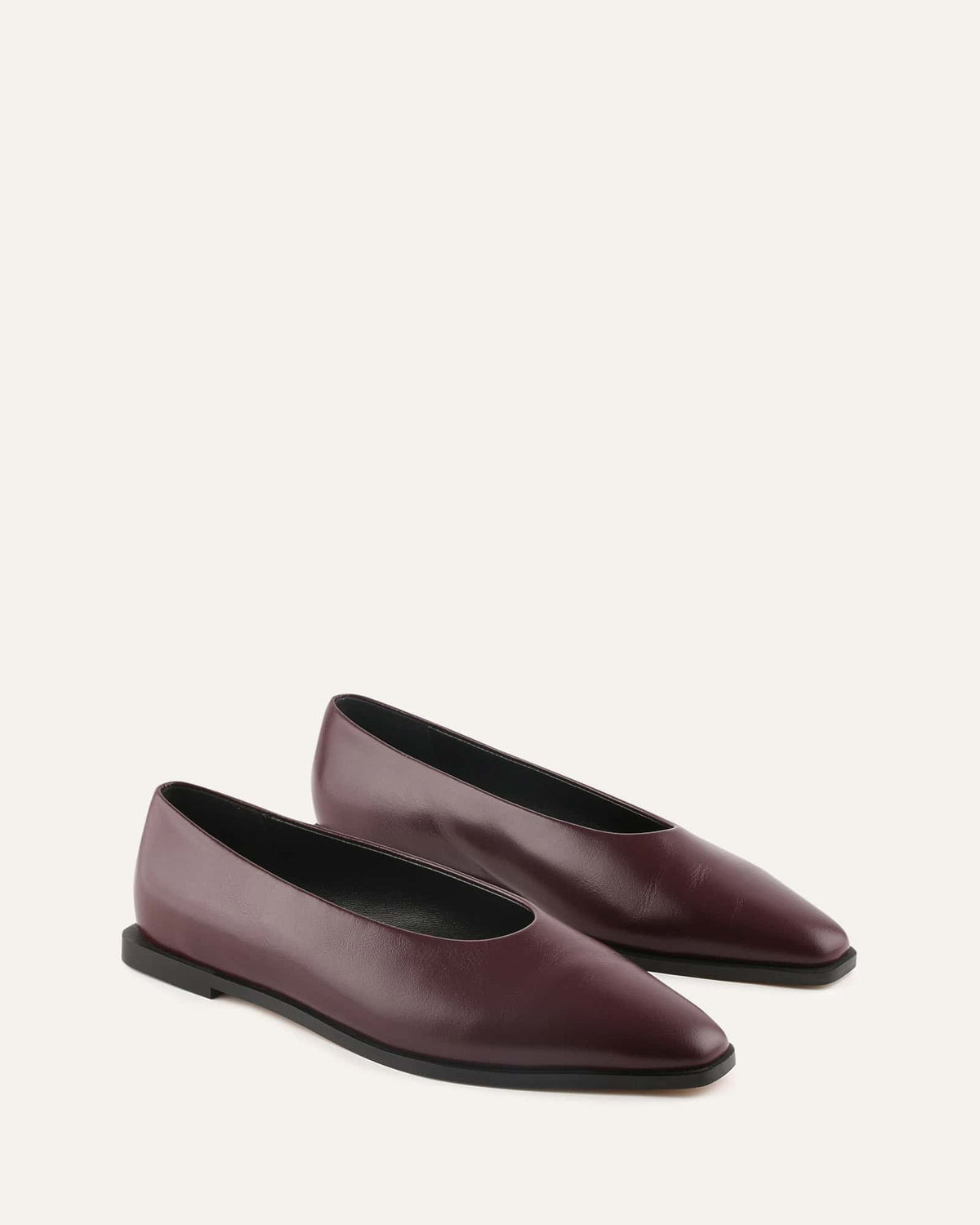 Pair of maroon pointed-toe flats on a light beige background