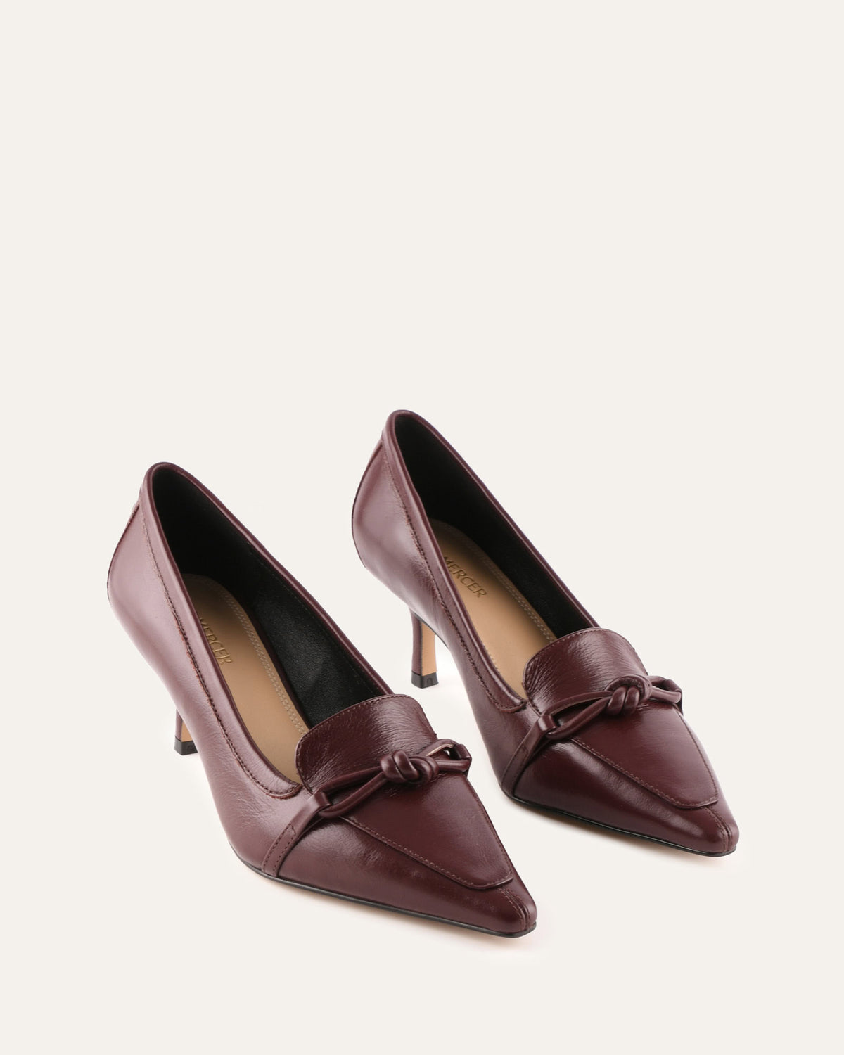 Pair of maroon high-heeled shoes with a bow on a light beige background