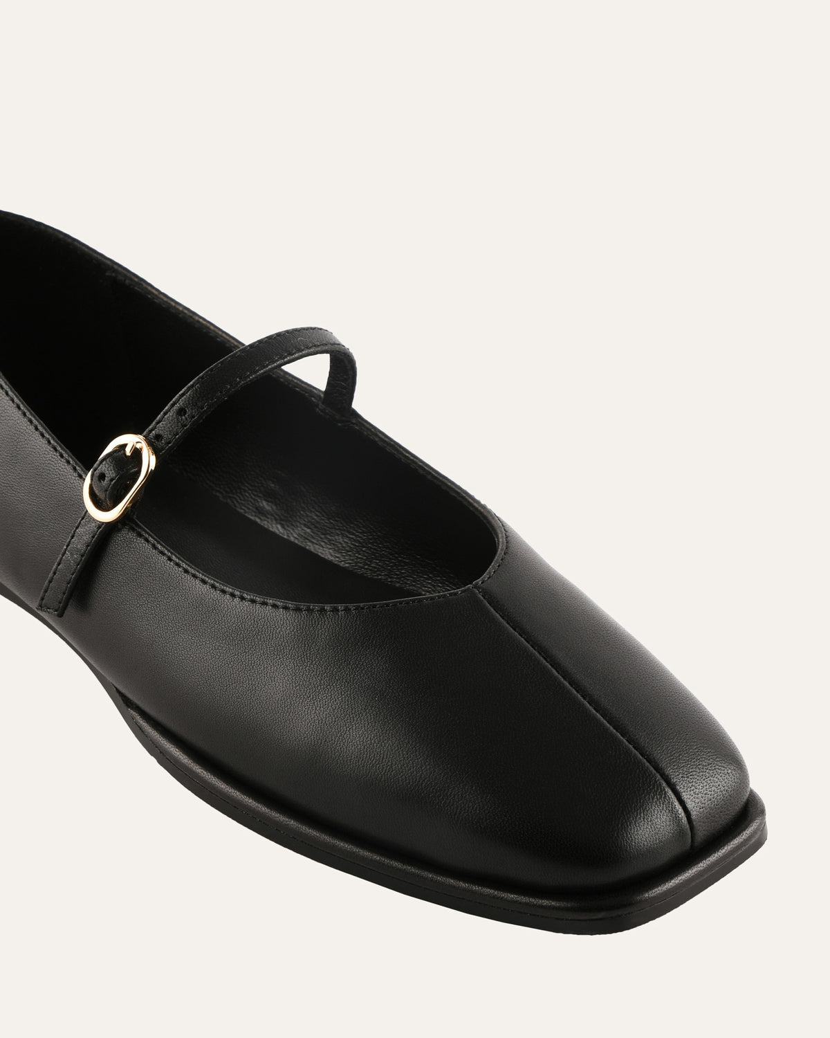 Black leather flat shoe with a strap on a light gray background