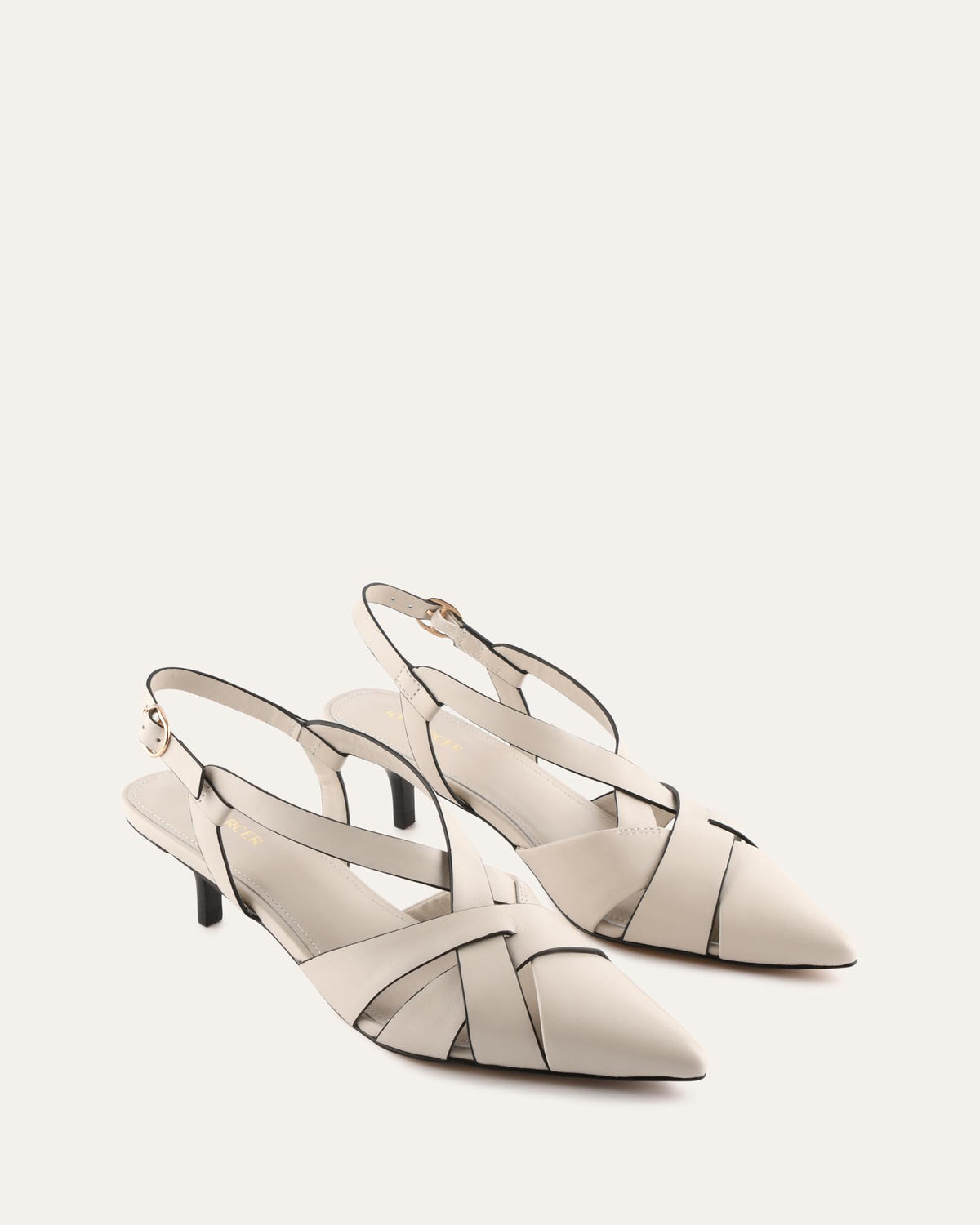 A pair of pointed-toe slingback heels in a light warm off-white leather with thin black trim and mid-height stiletto heels, photographed on a clean off-white background.