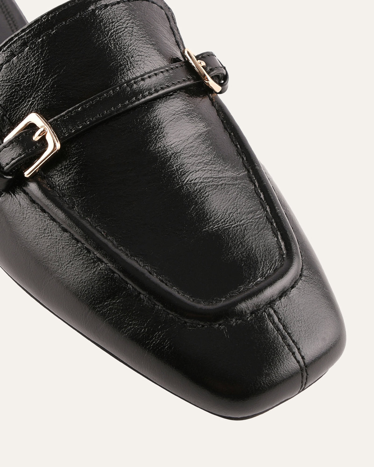 Black leather loafer with gold buckle on a white background