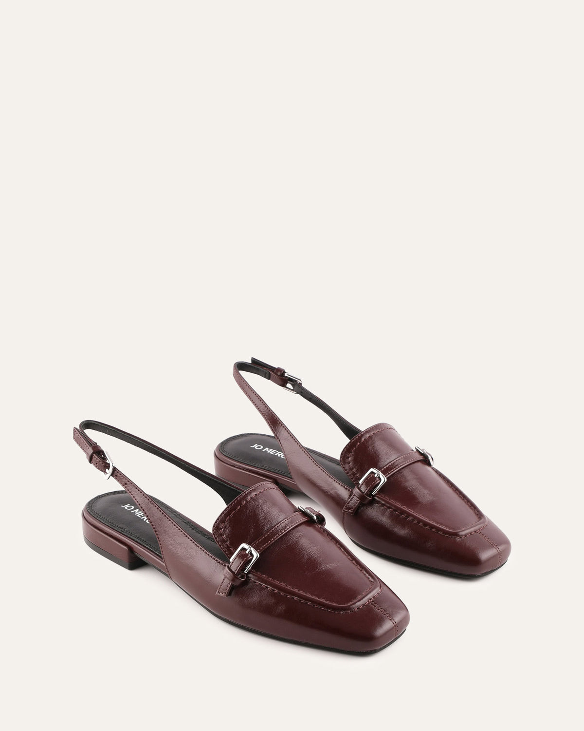 Pair of maroon loafers with a buckle on a light gray background