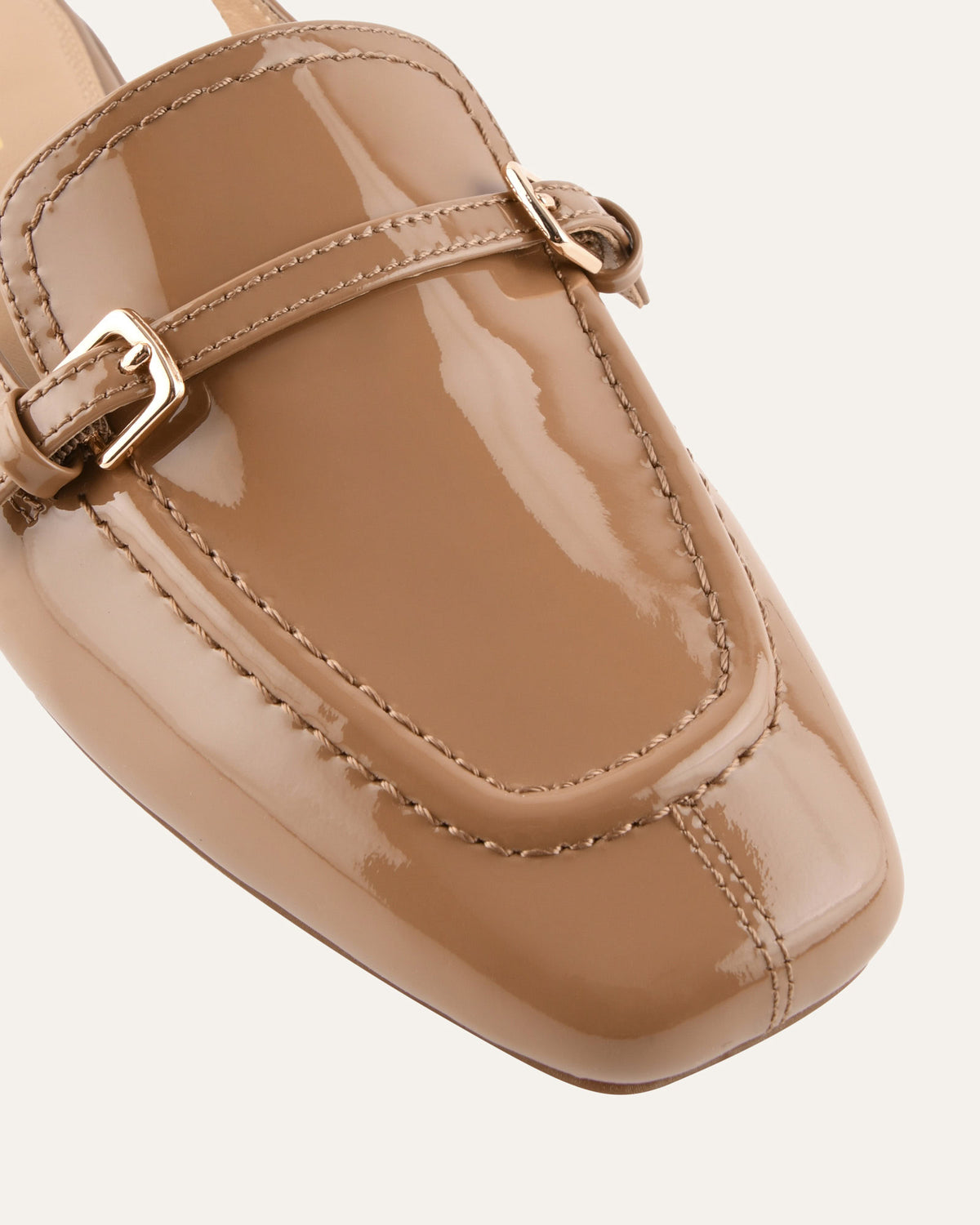 Beige patent leather loafer with a buckle on a white background