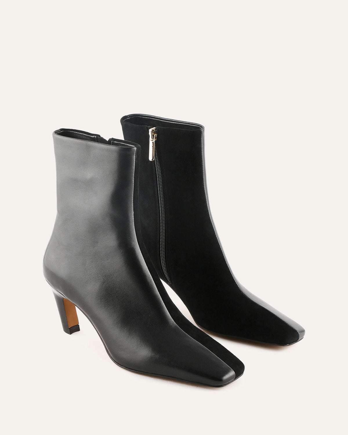 Pair of black ankle boots with a zipper on a light gray background