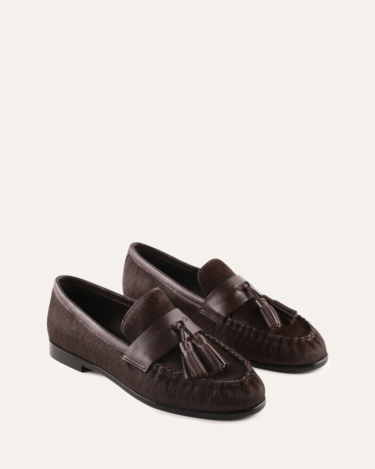 Pair of brown loafers with tassels on a light beige background