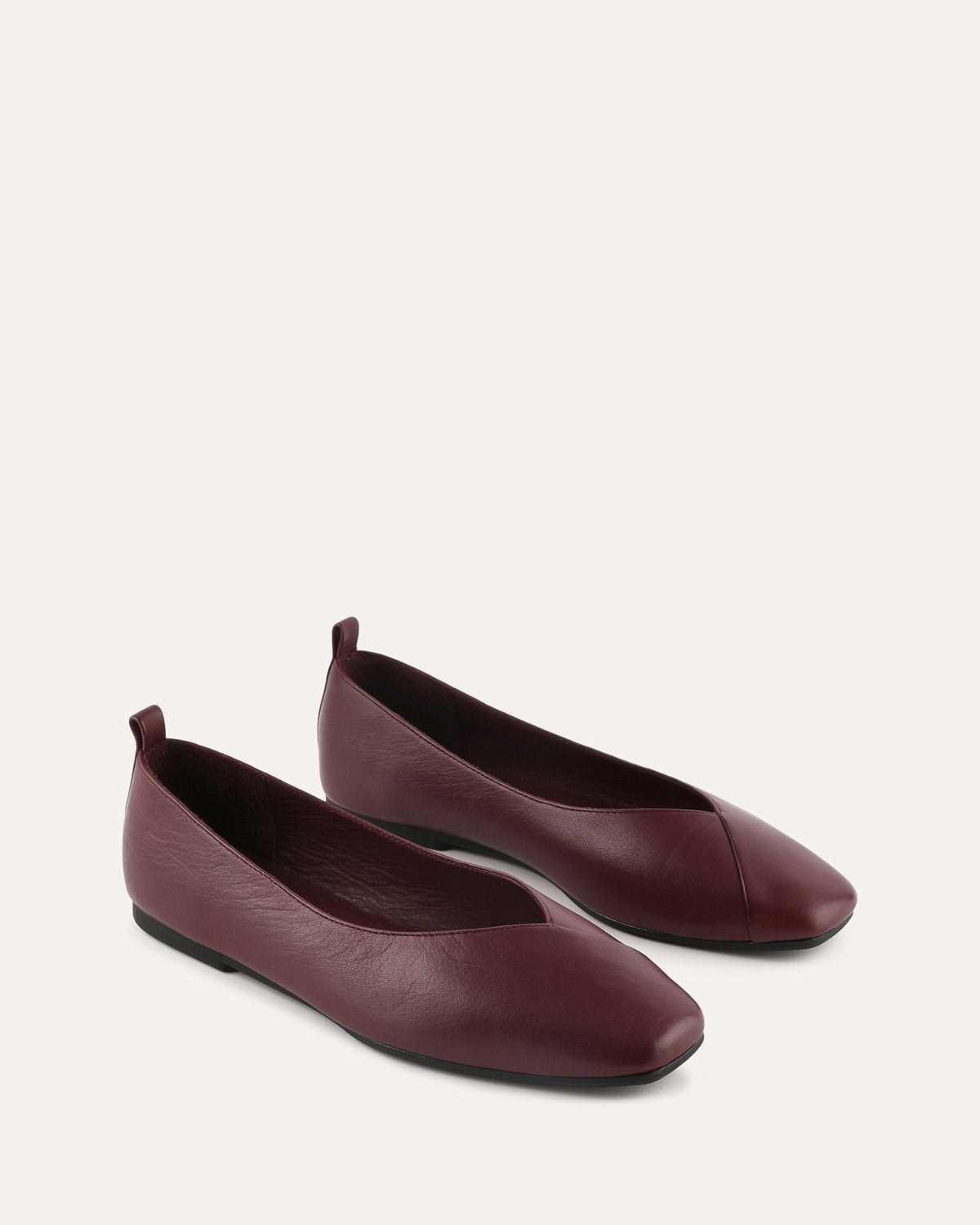 Pair of maroon flat shoes on a light beige background