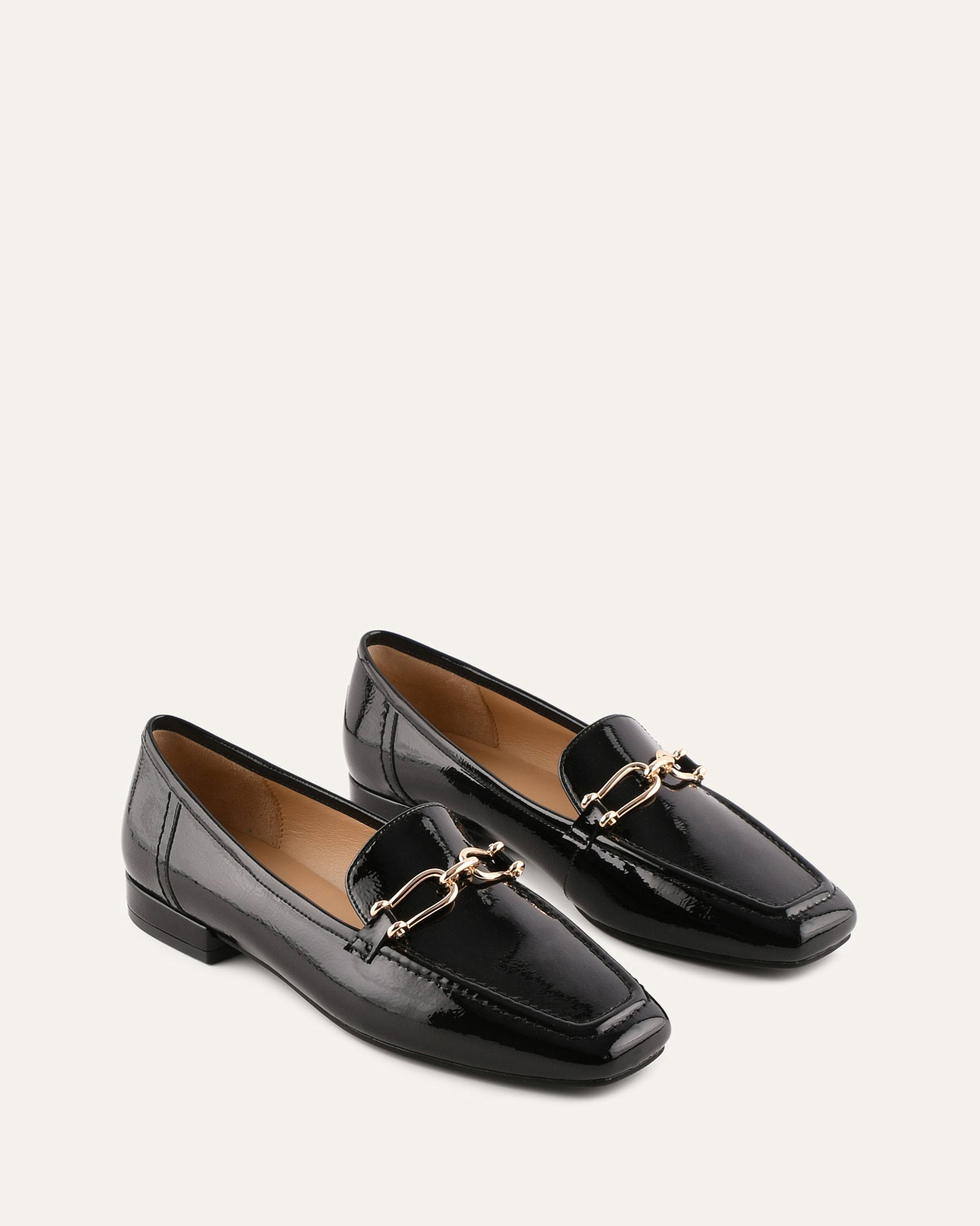 Black patent leather loafer with a gold buckle on a white background