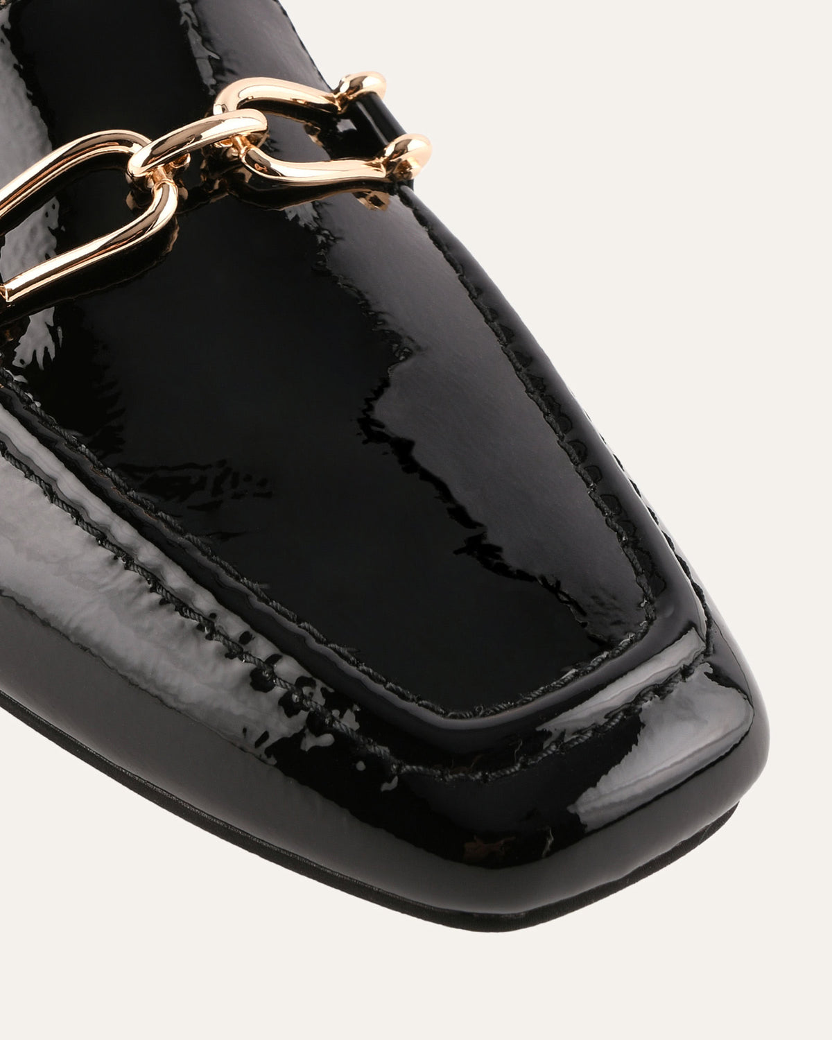 Black patent leather loafer with gold chain detail on a white background