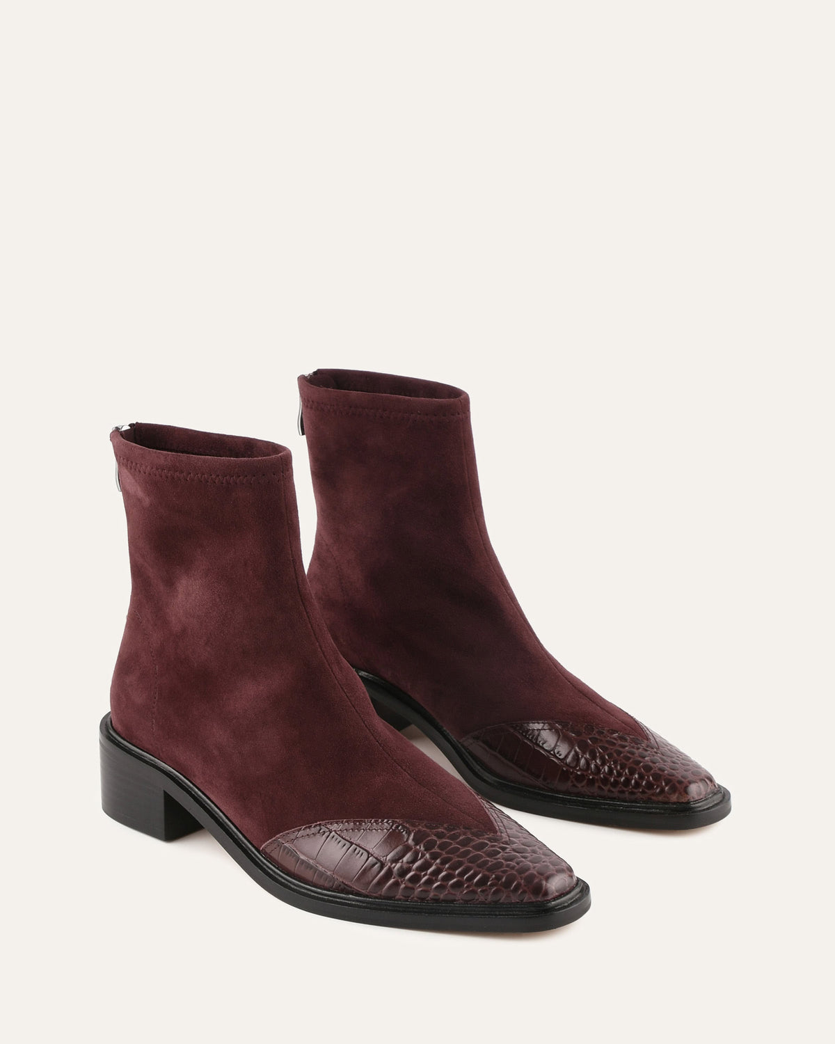 Pair of maroon suede ankle boots with a textured toe on a light beige background
