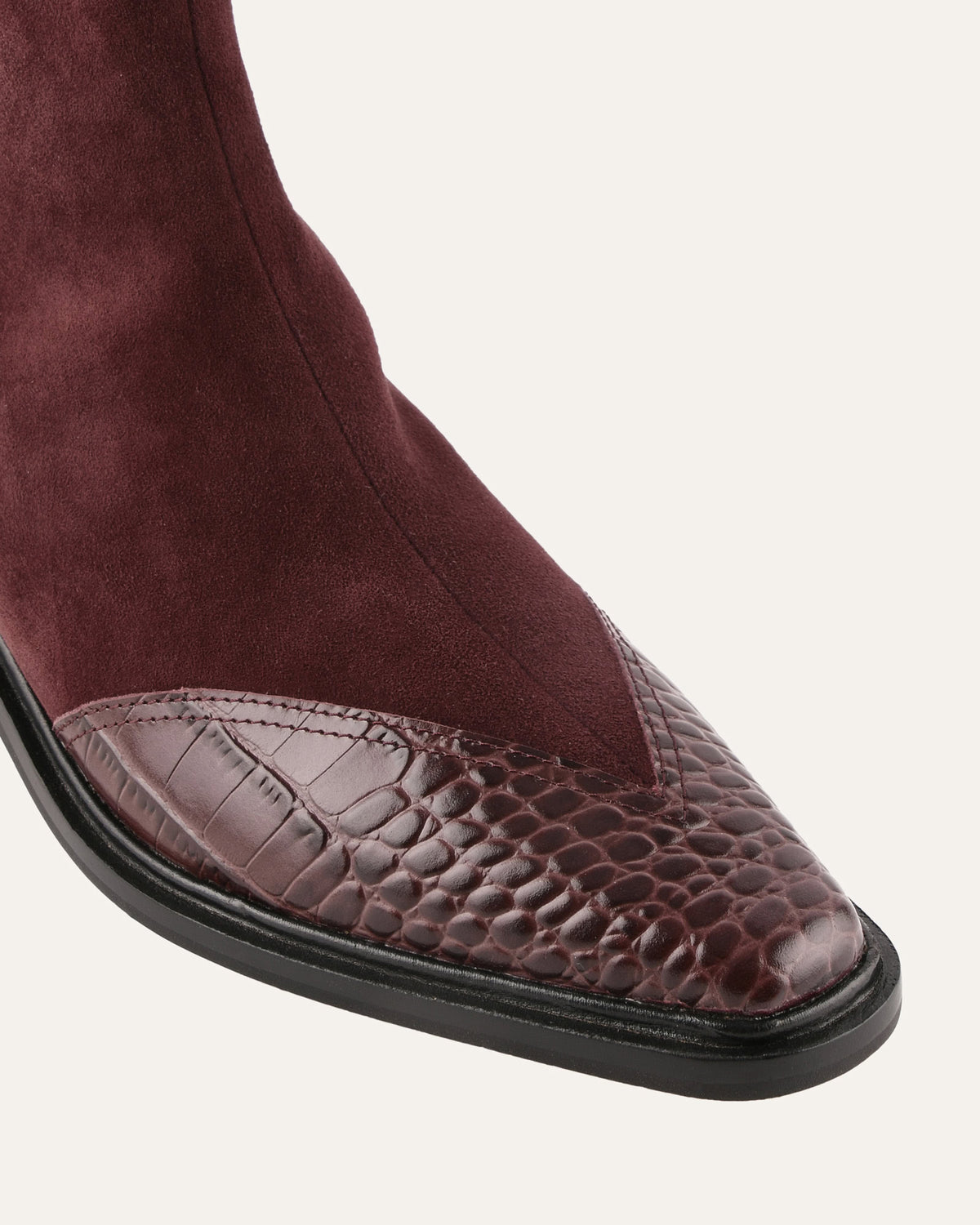 Close-up of a burgundy suede boot with a crocodile-patterned toe cap on a white background