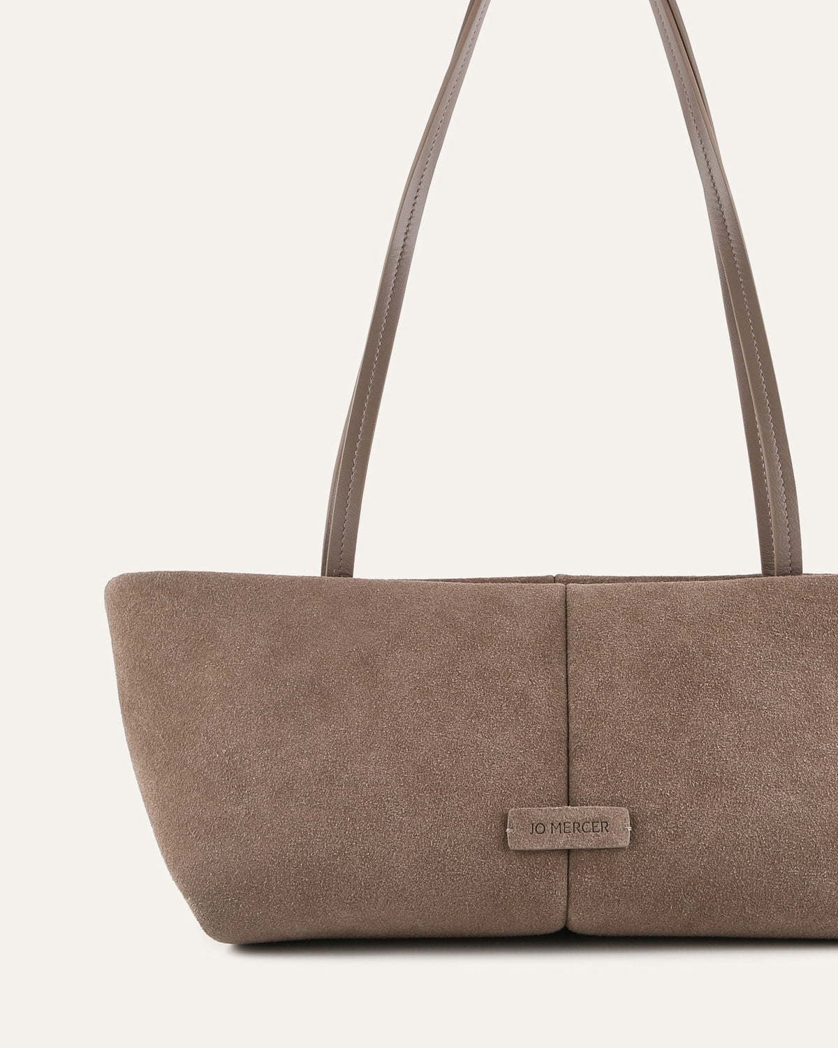 Brown suede handbag with a visible brand label on a light beige background
