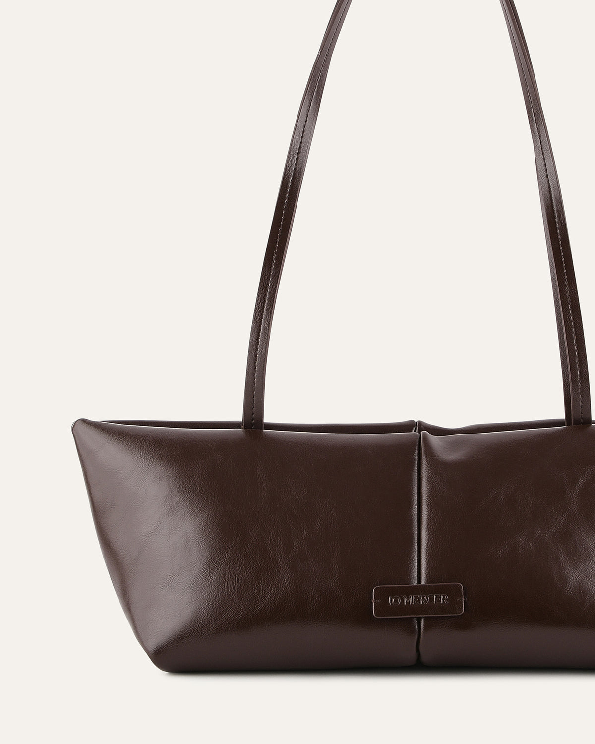 Brown leather handbag with a visible brand label on a light beige background