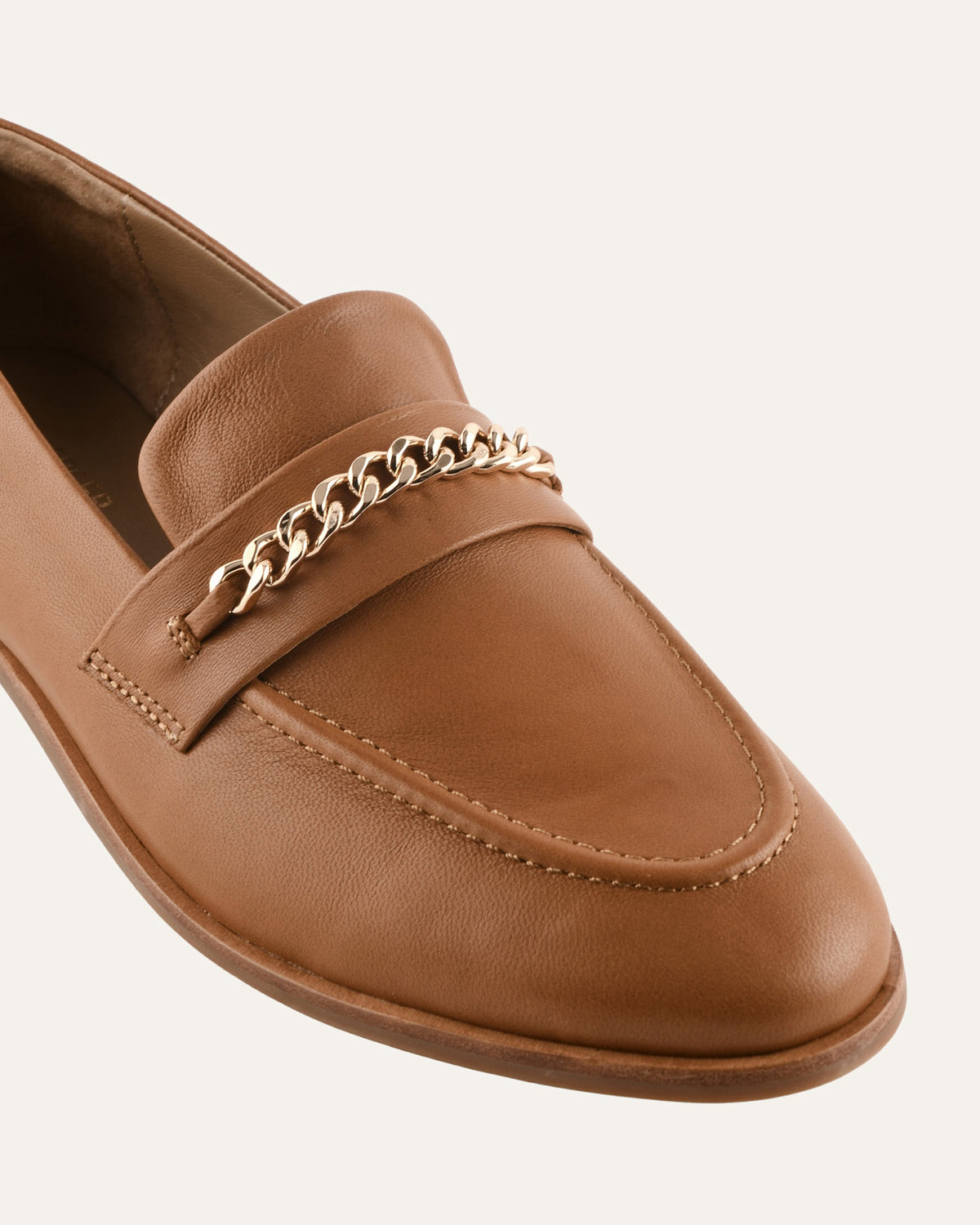 Brown loafer shoe with gold chain detail on a white background