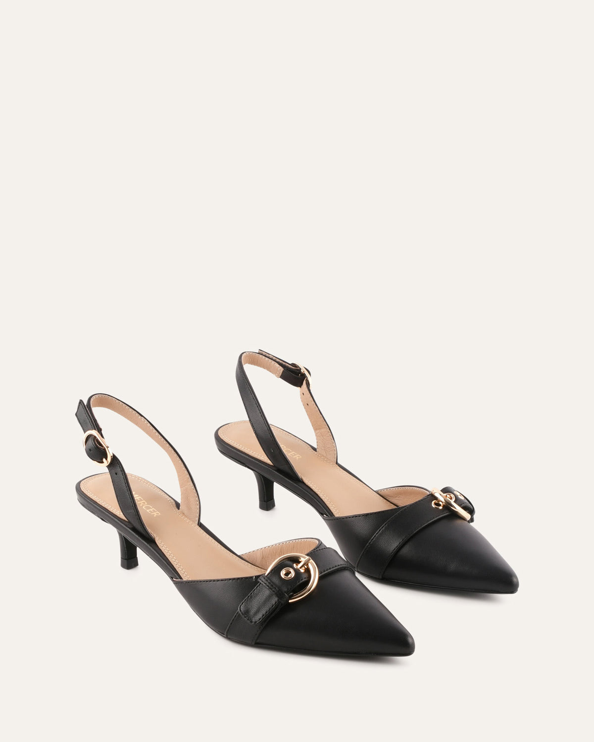 Black high-heeled shoes with gold buckles on a light beige background