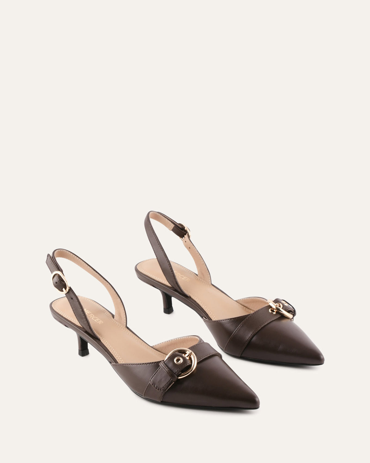 Pair of brown high-heeled shoes with a decorative buckle on a light beige background