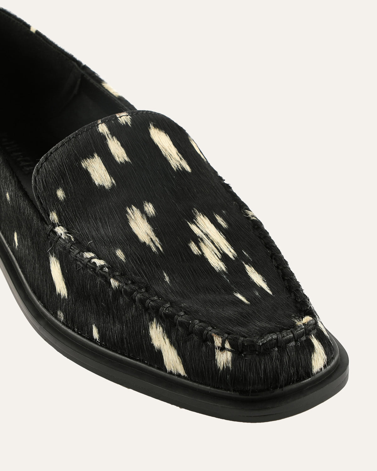 Black loafer with white cowhide pattern on a light gray background