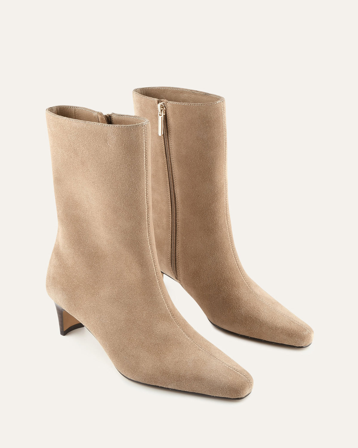 Pair of beige ankle boots with a zipper on a light gray background