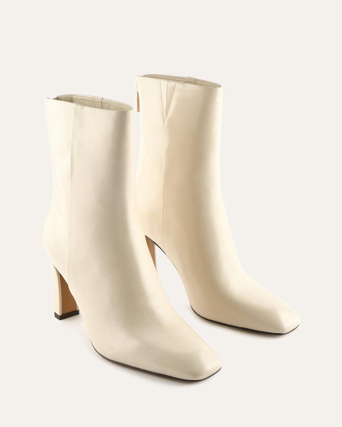 Pair of cream-colored high-heeled ankle boots on a light gray background