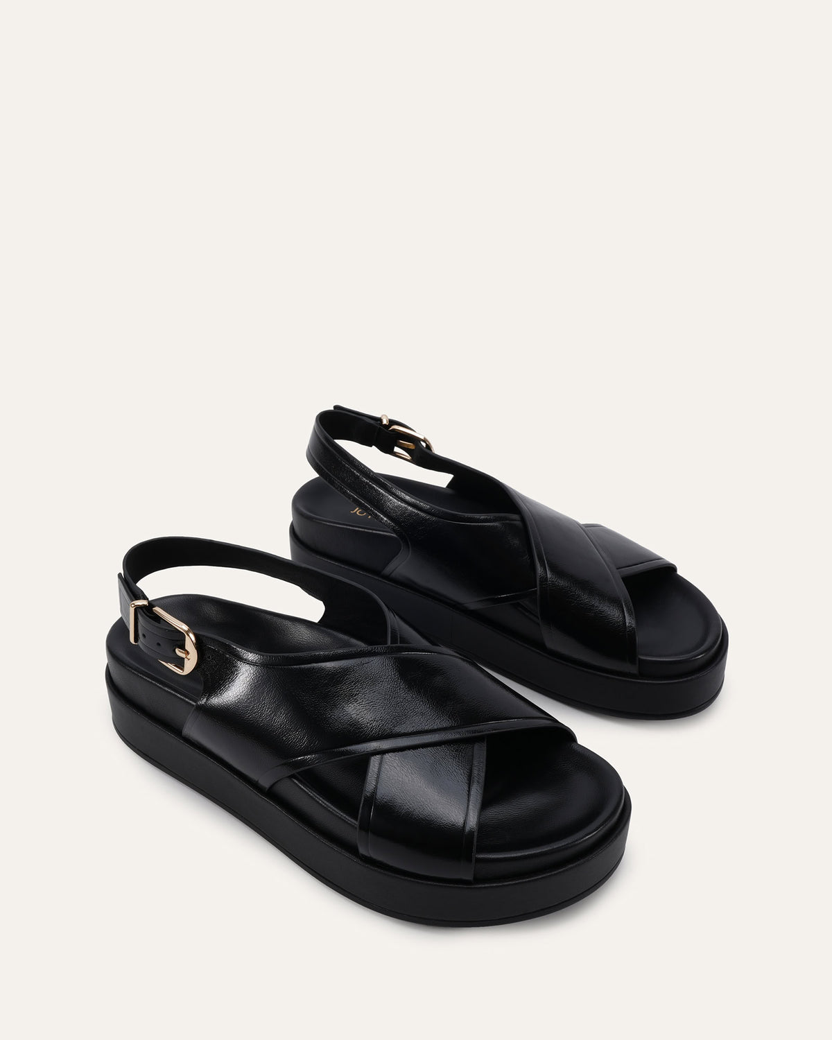 A pair of black leather platform sandals with crisscross straps and ankle buckles, photographed on a clean off-white background.