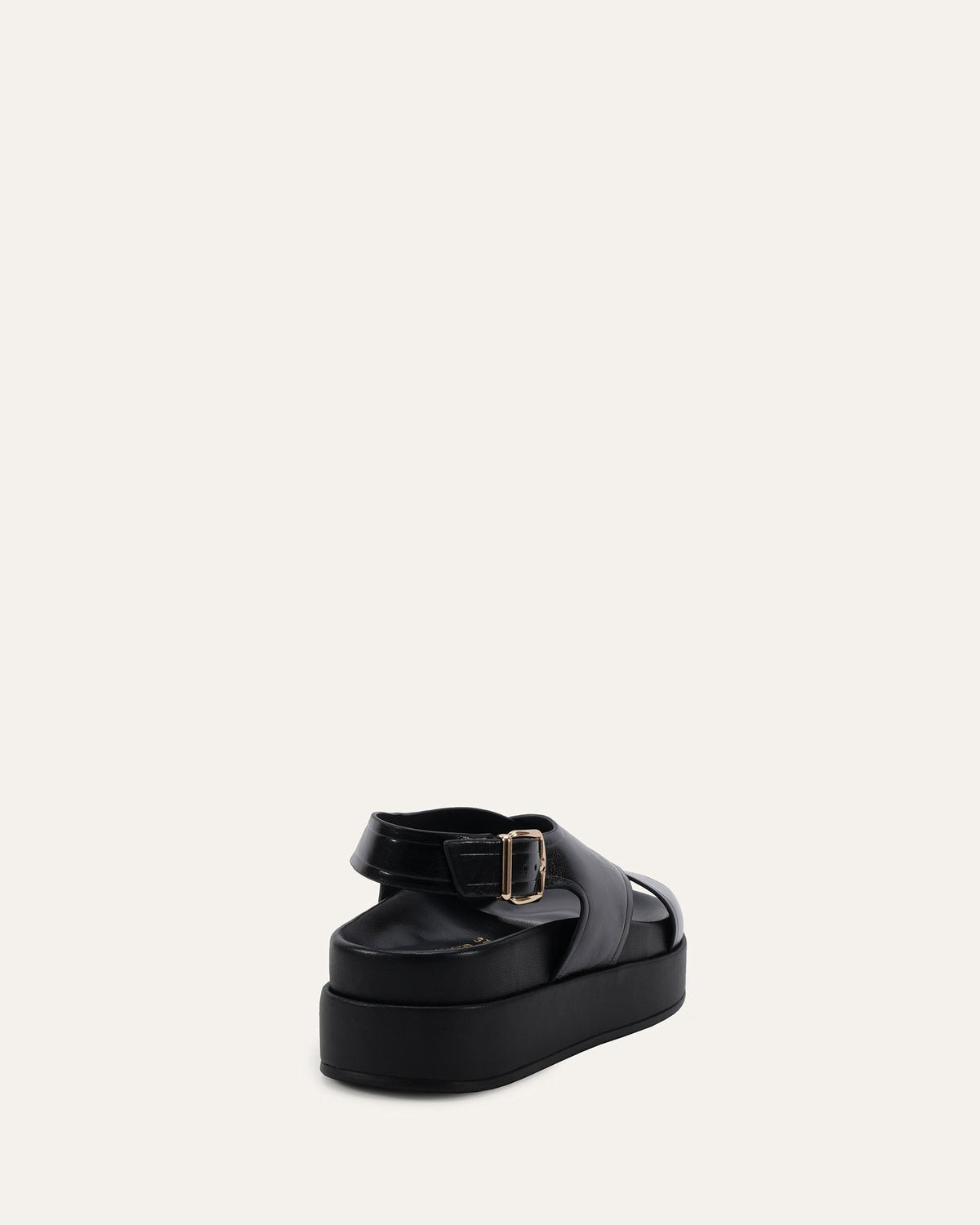 A single black platform sandal with a wide strap and a gold-tone buckle, shown from a rear three-quarter angle against a solid off-white background.