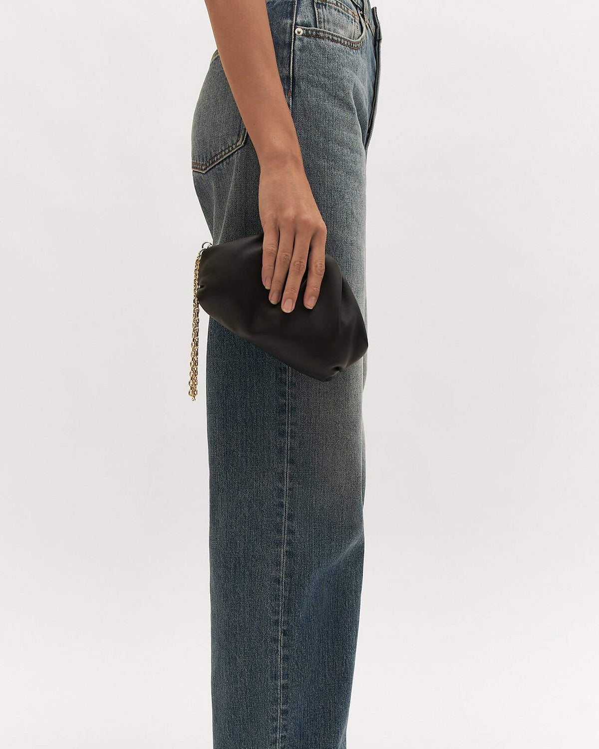 Person holding a black clutch with a gold chain against a white background