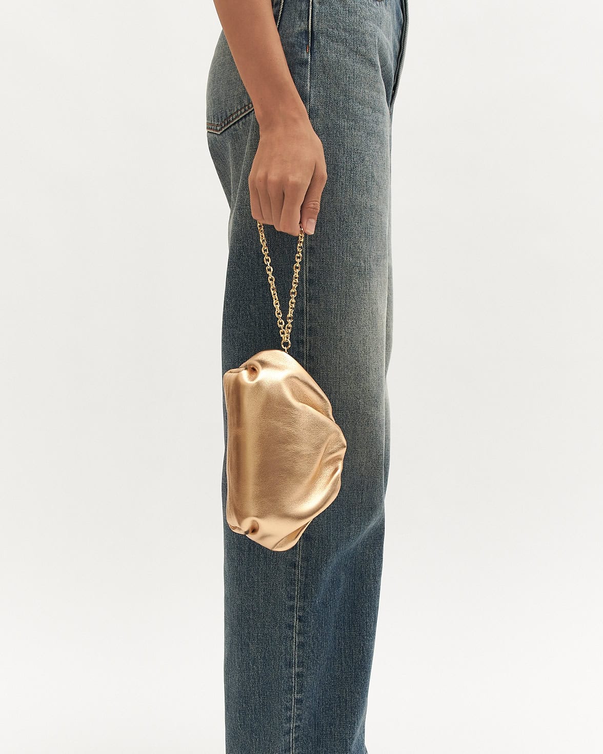 Gold clutch held by a person wearing blue jeans on a white background