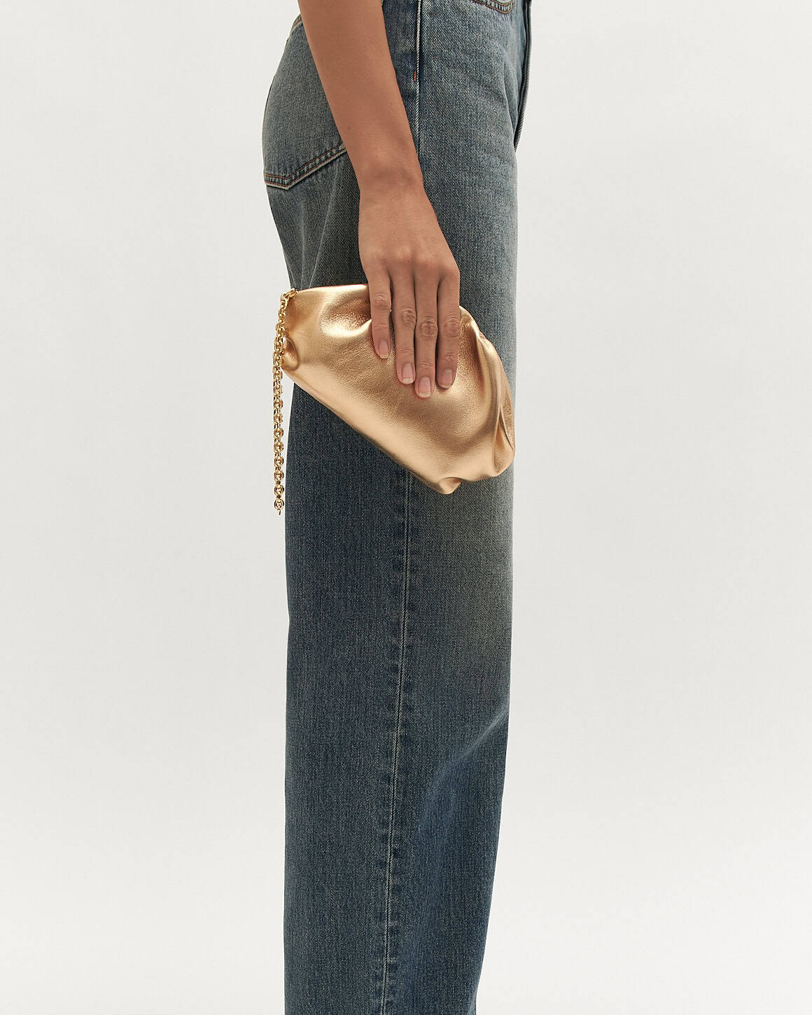 Gold clutch held by a person wearing blue jeans on a white background