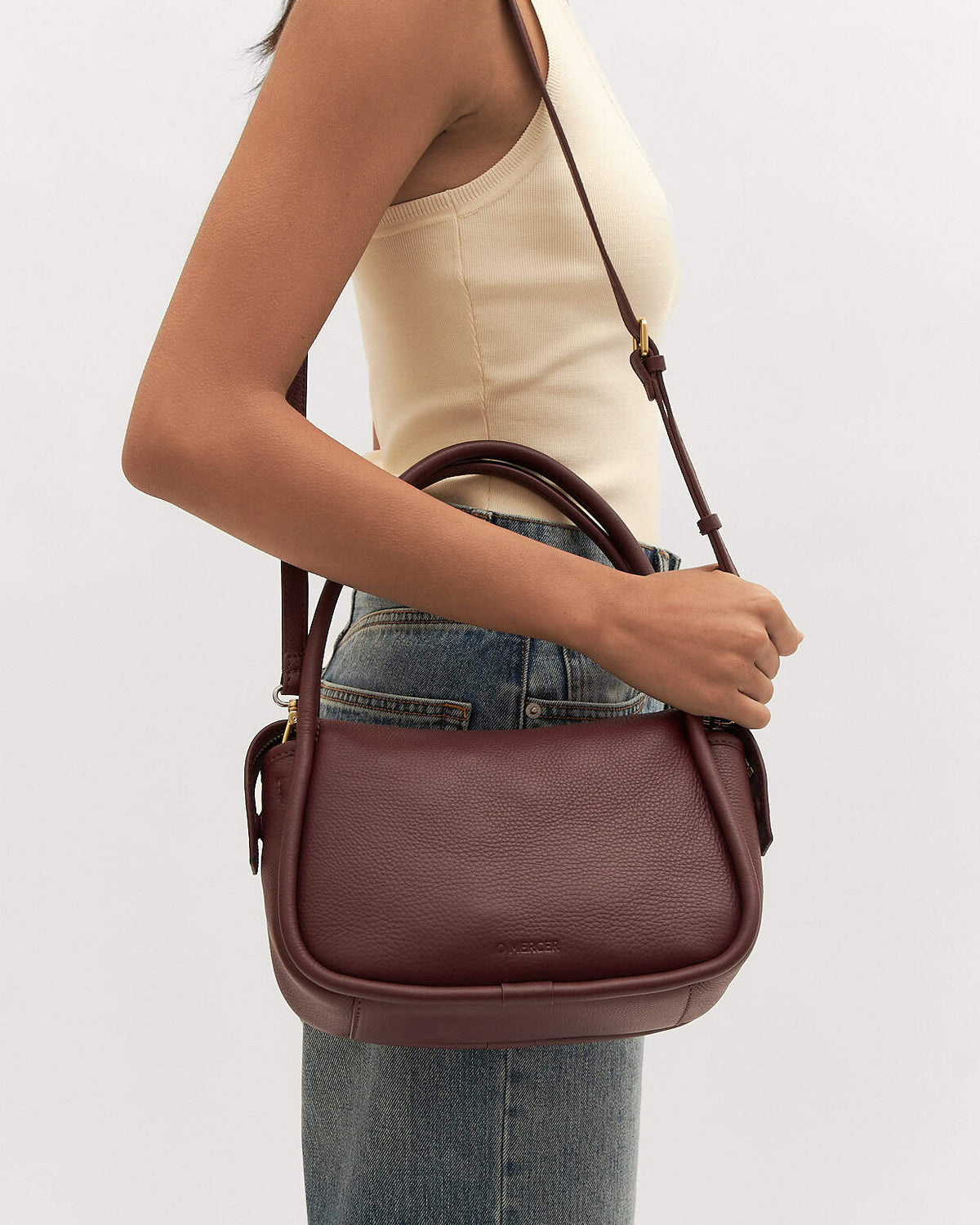 Brown leather handbag worn by a person on a light gray background