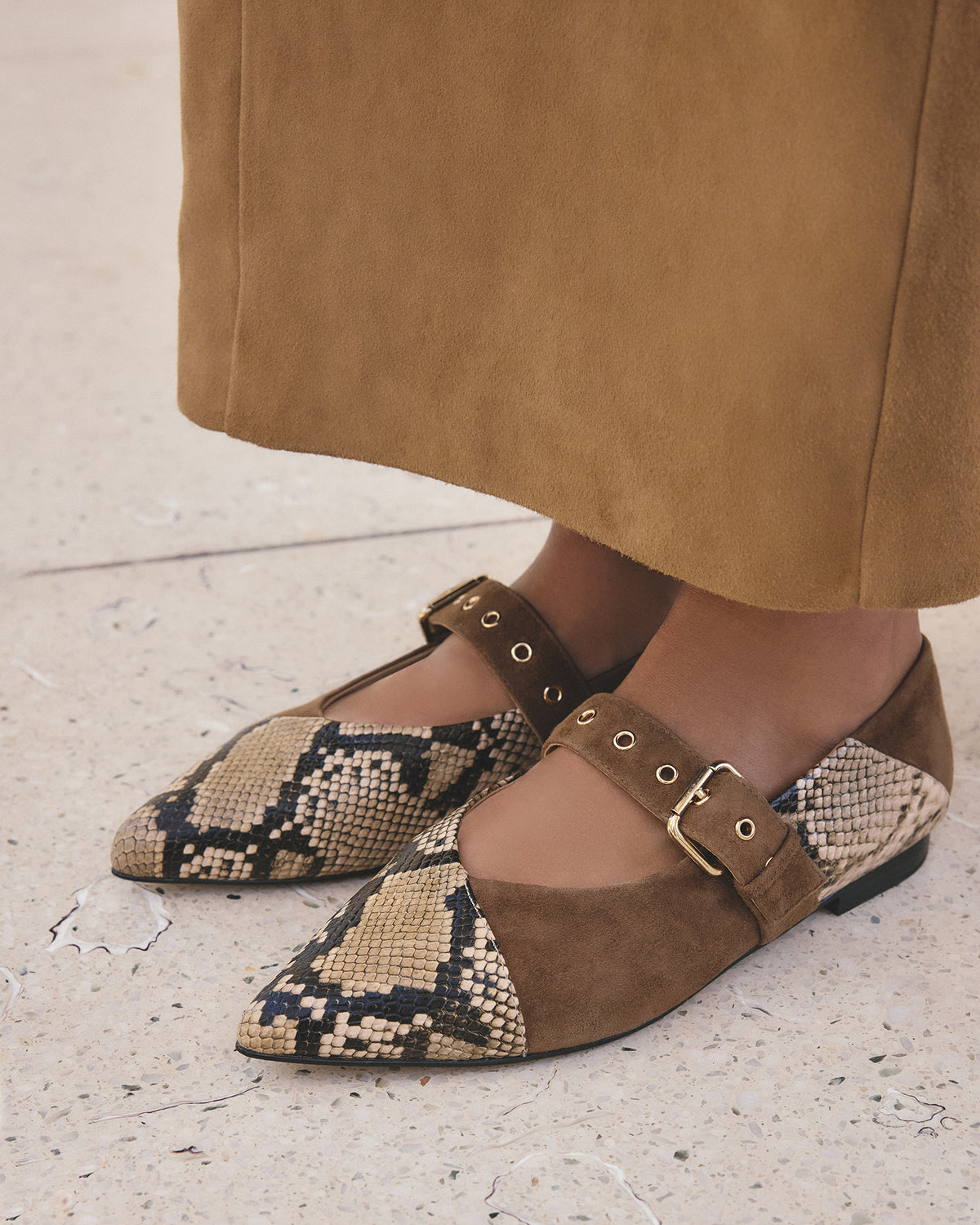 Brown and snake print flats worn with a tan skirt on a light background