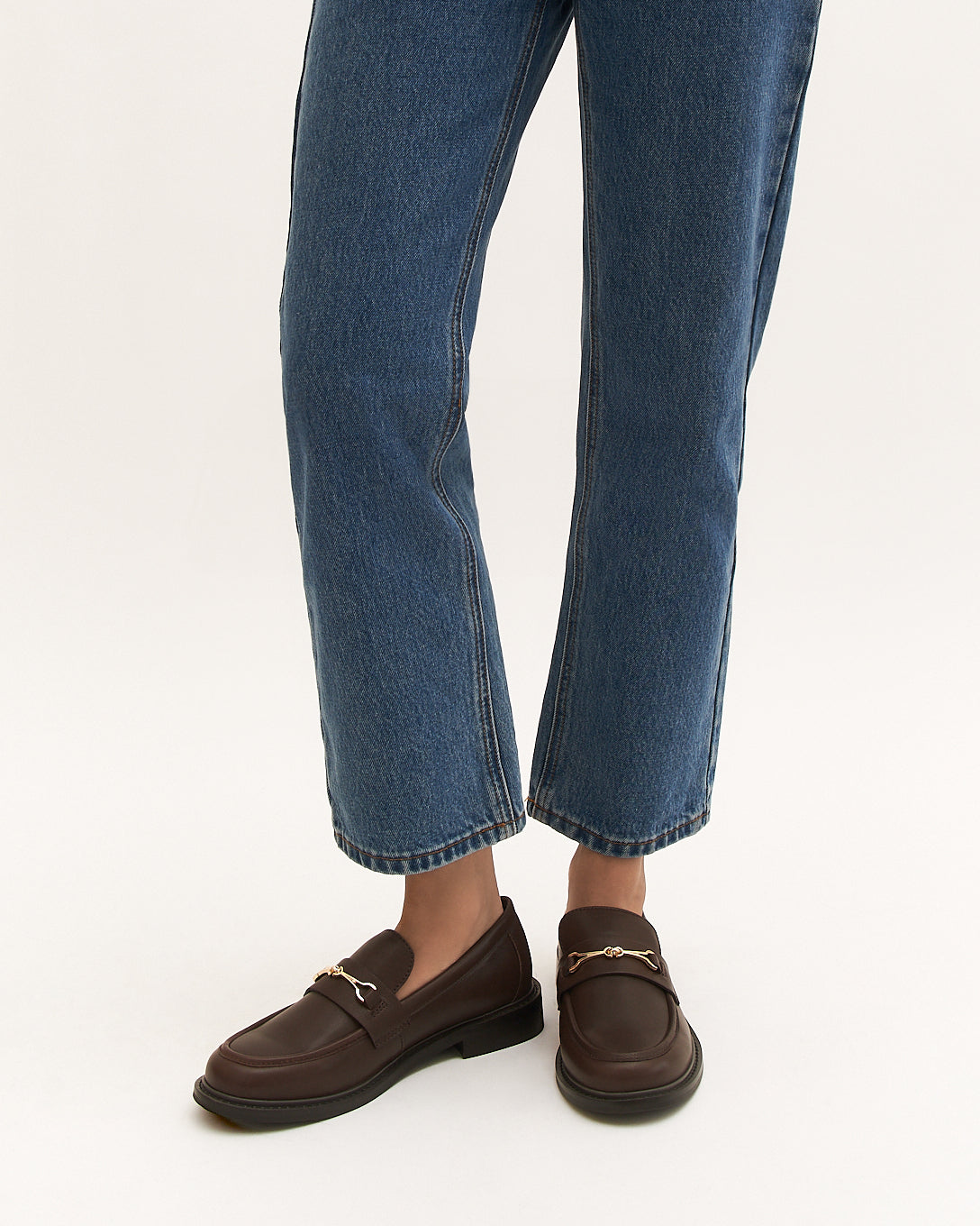 Brown leather loafer with a gold buckle on a white background