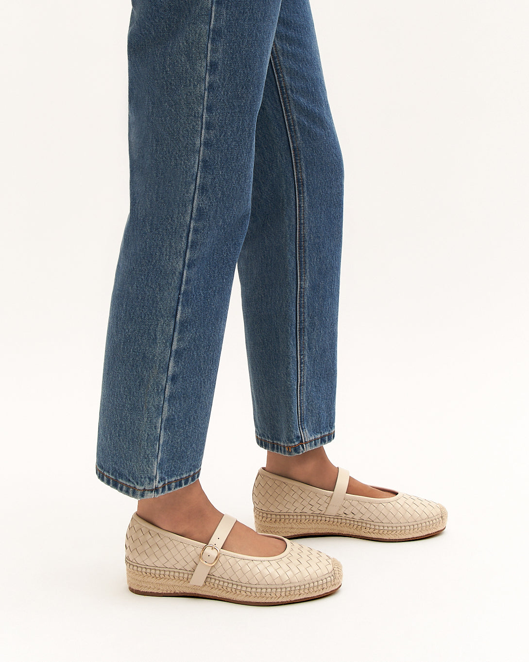 Person wearing blue jeans and beige espadrille shoes on a white background