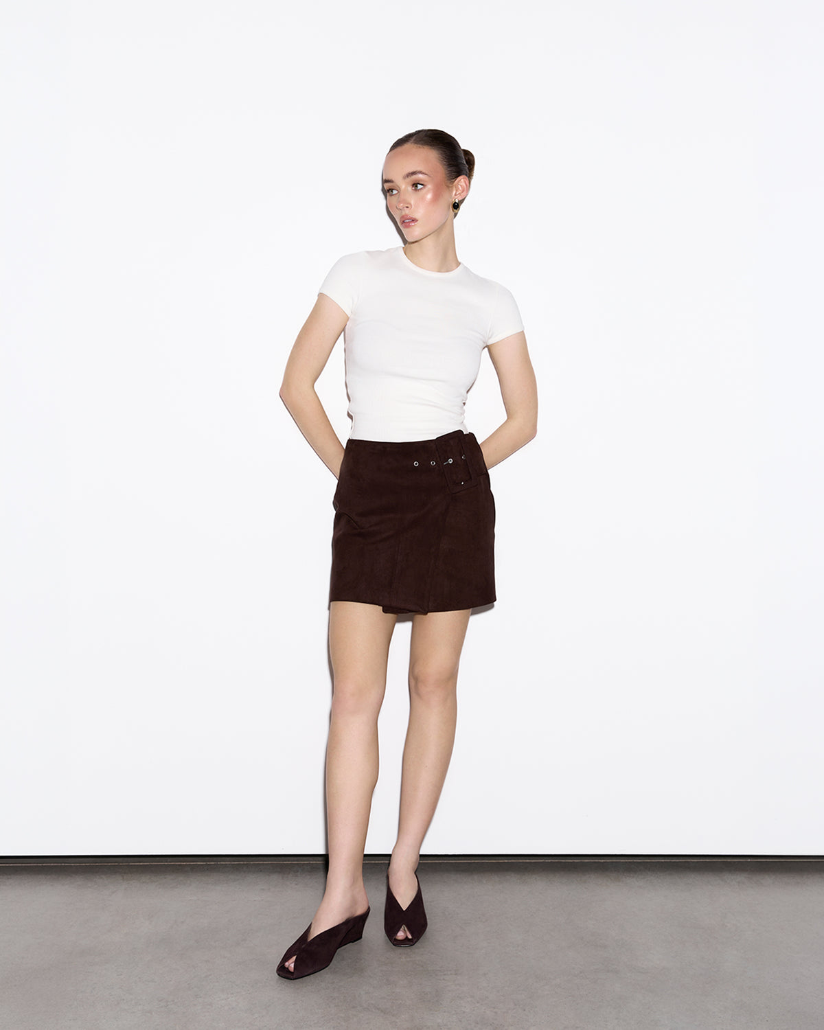 Woman wearing a white top and brown skirt against a plain background