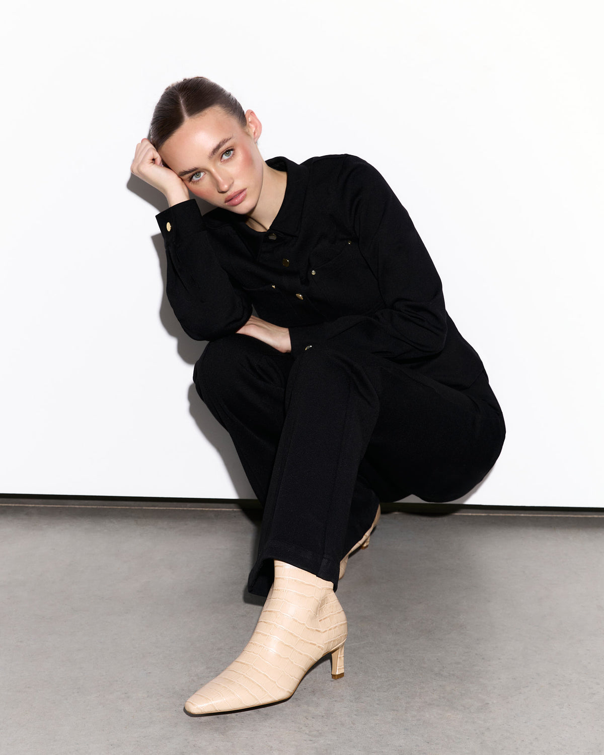 Woman in black outfit with beige croc boots sitting on a white floor.