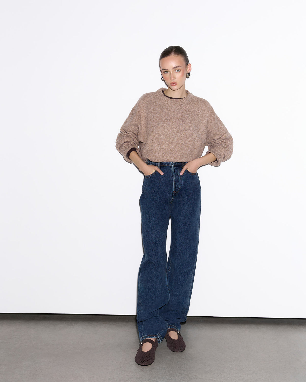 Person wearing a brown sweater and blue jeans against a white background